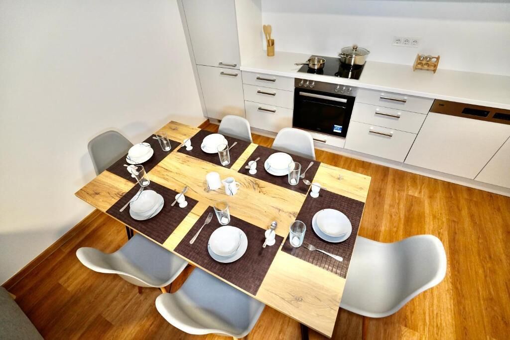 A modern kitchen with white cabinets, a black oven, and a dining area with a wooden table set for four.
