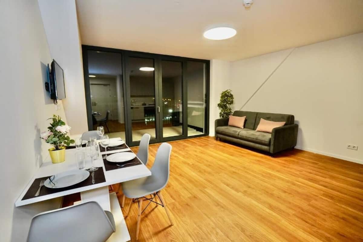 En moderne stue med spiseplads, trægulv, sofa og en skydedør til en balkon.