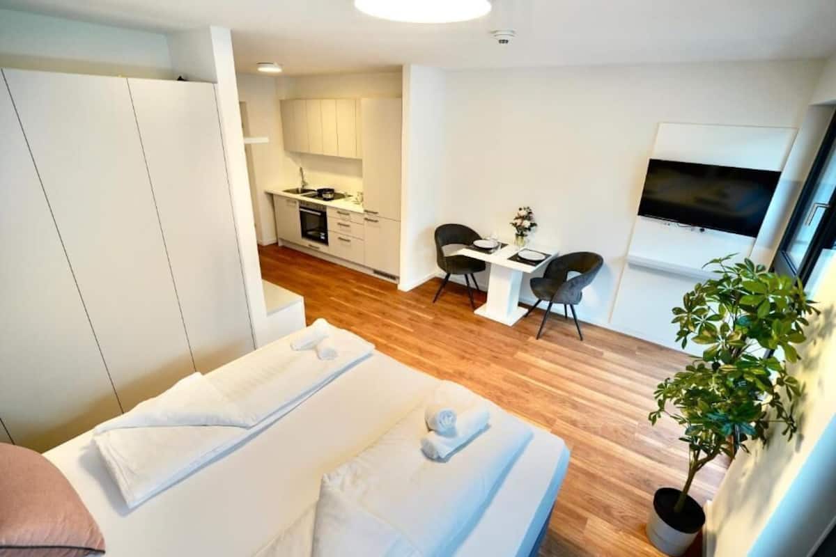Et moderne hotelværelse med seng, et lille tekøkken, spiseplads og TV.