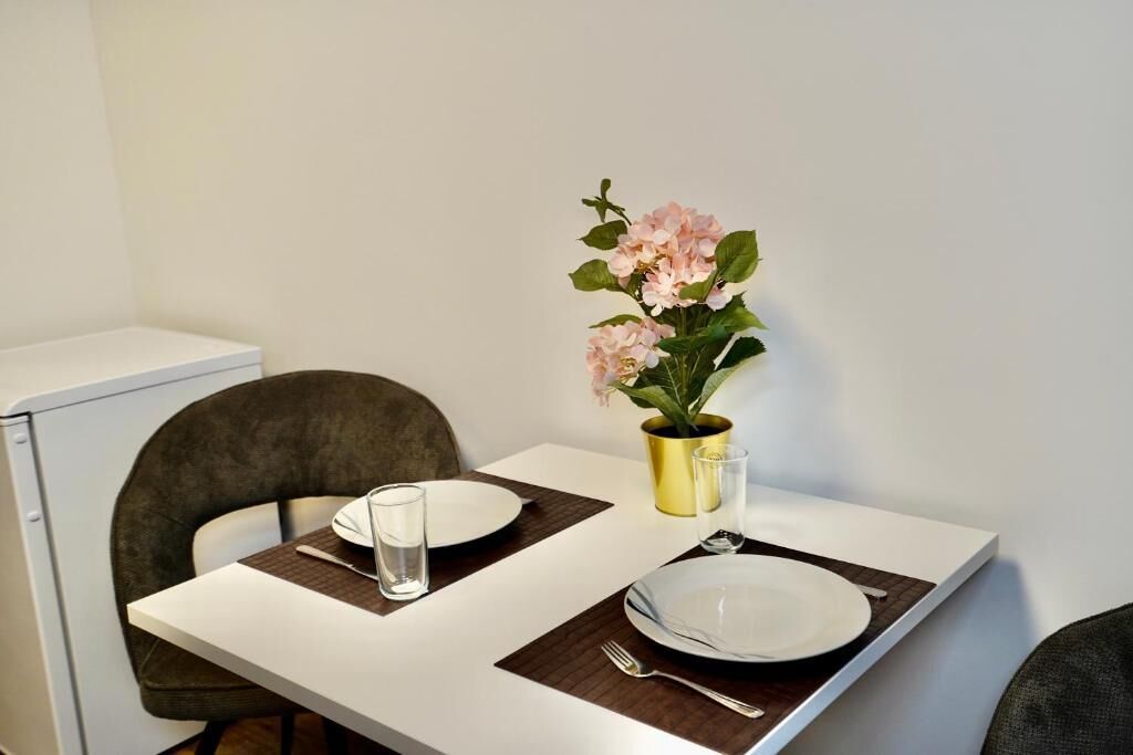 A dining table with two plates, cutlery, and a glass of water. A vase with flowers is on the table.