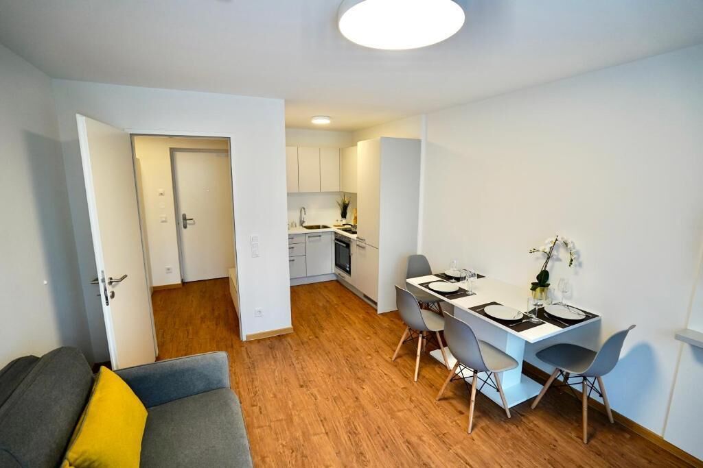 Un apartamento moderno con comedor, kitchenette y sala de estar con sofá y almohadón amarillo.