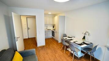 Un apartamento moderno con comedor, kitchenette y sala de estar con sofá y almohadón amarillo.