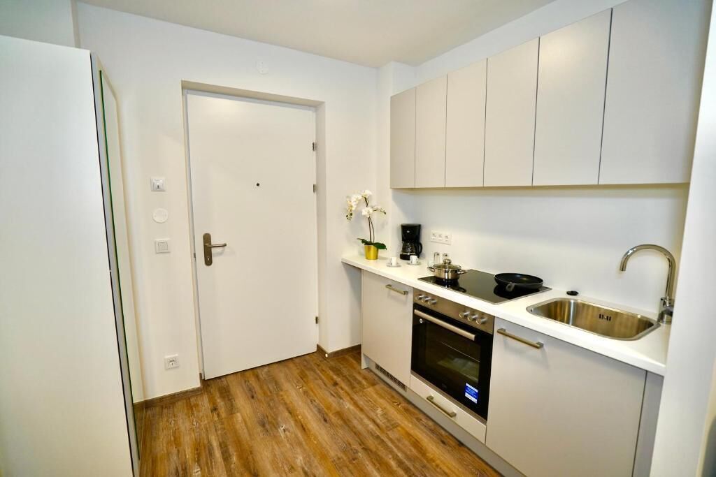 Una cucina compatta con mobili bianchi, un lavello in acciaio inossidabile e un forno integrato.