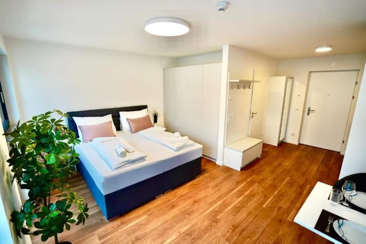 Et moderne soveværelse med seng, garderobe, siddeplads og en plante.