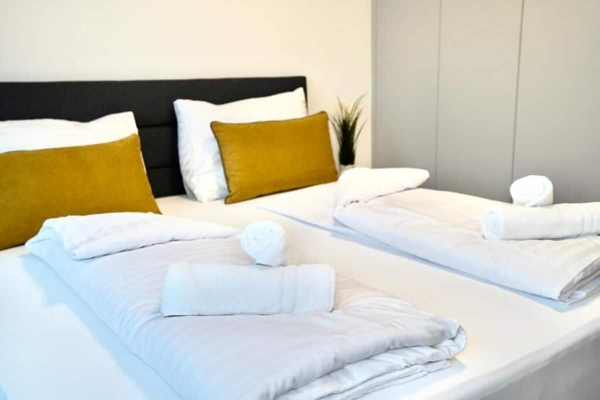 Et hotelværelse med to senge, begge med hvide hør og en enkelt brun pude.