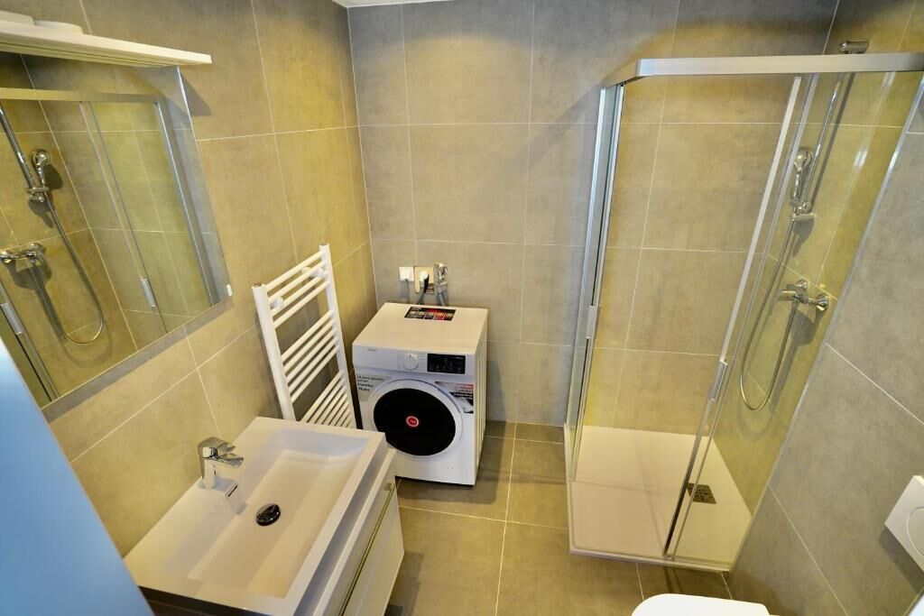 A compact bathroom with a shower, a sink, and a washing machine.