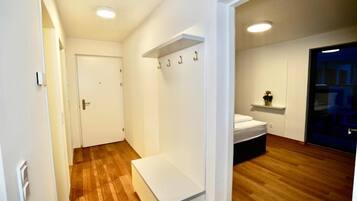 Une pièce moderne et bien éclairée, dotée d’un plancher en bois, d’un banc blanc, d’un lit et d’une porte donnant sur une autre pièce.