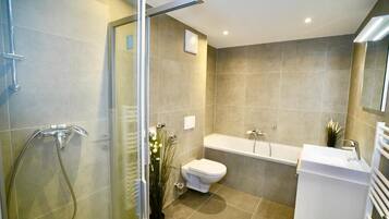 Une salle de bain moderne avec une douche à parois de verre, des toilettes blanches, une baignoire et un lavabo blanc.