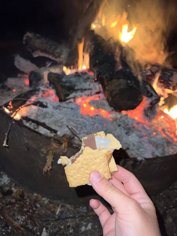 A hand holding a partially eaten chocolate bar with a campfire in the background. - Family Memories on Minnesota’s Greatest Lake! (Onamia)