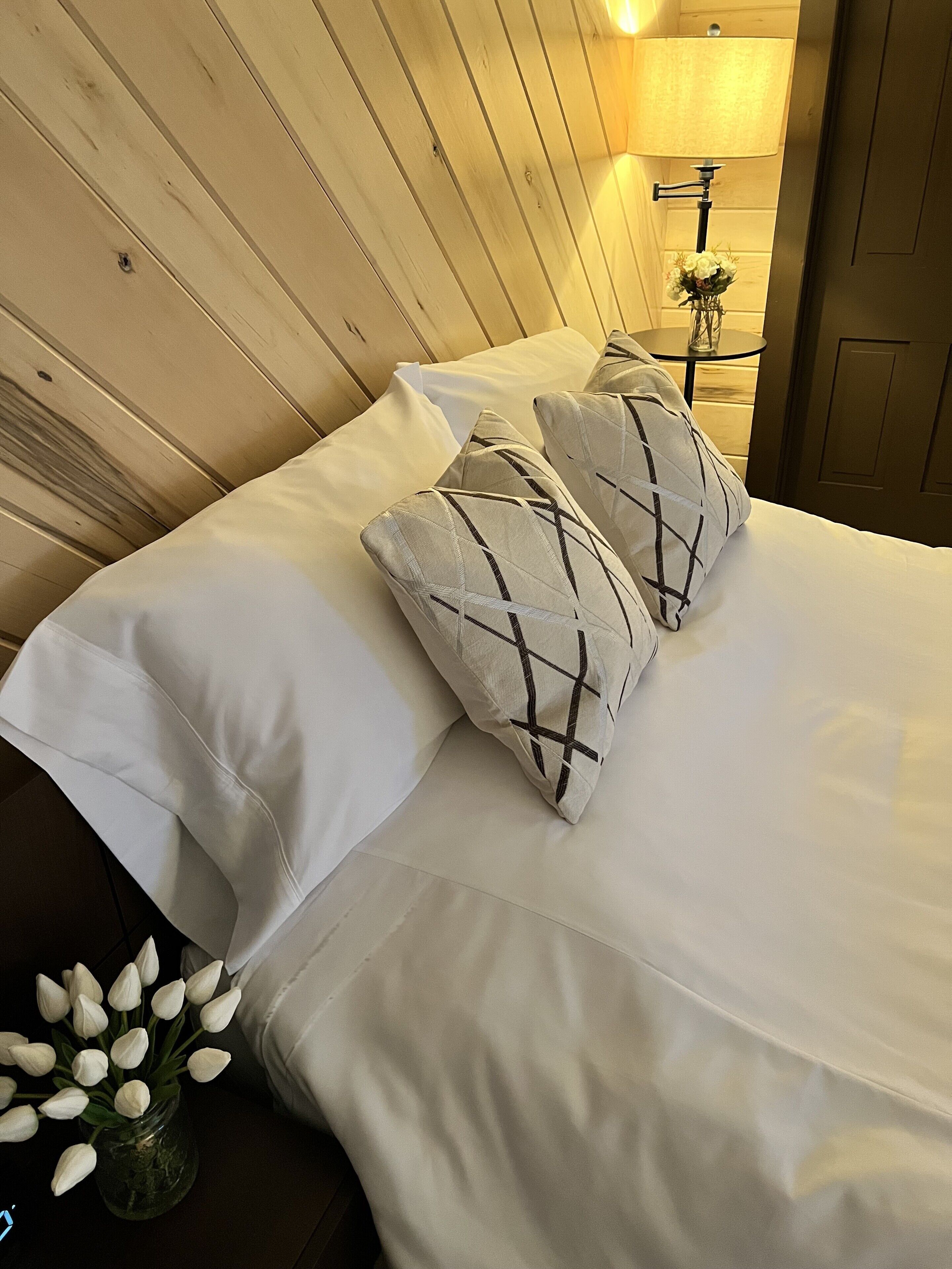 A bed with white linens and two decorative pillows with a geometric pattern.