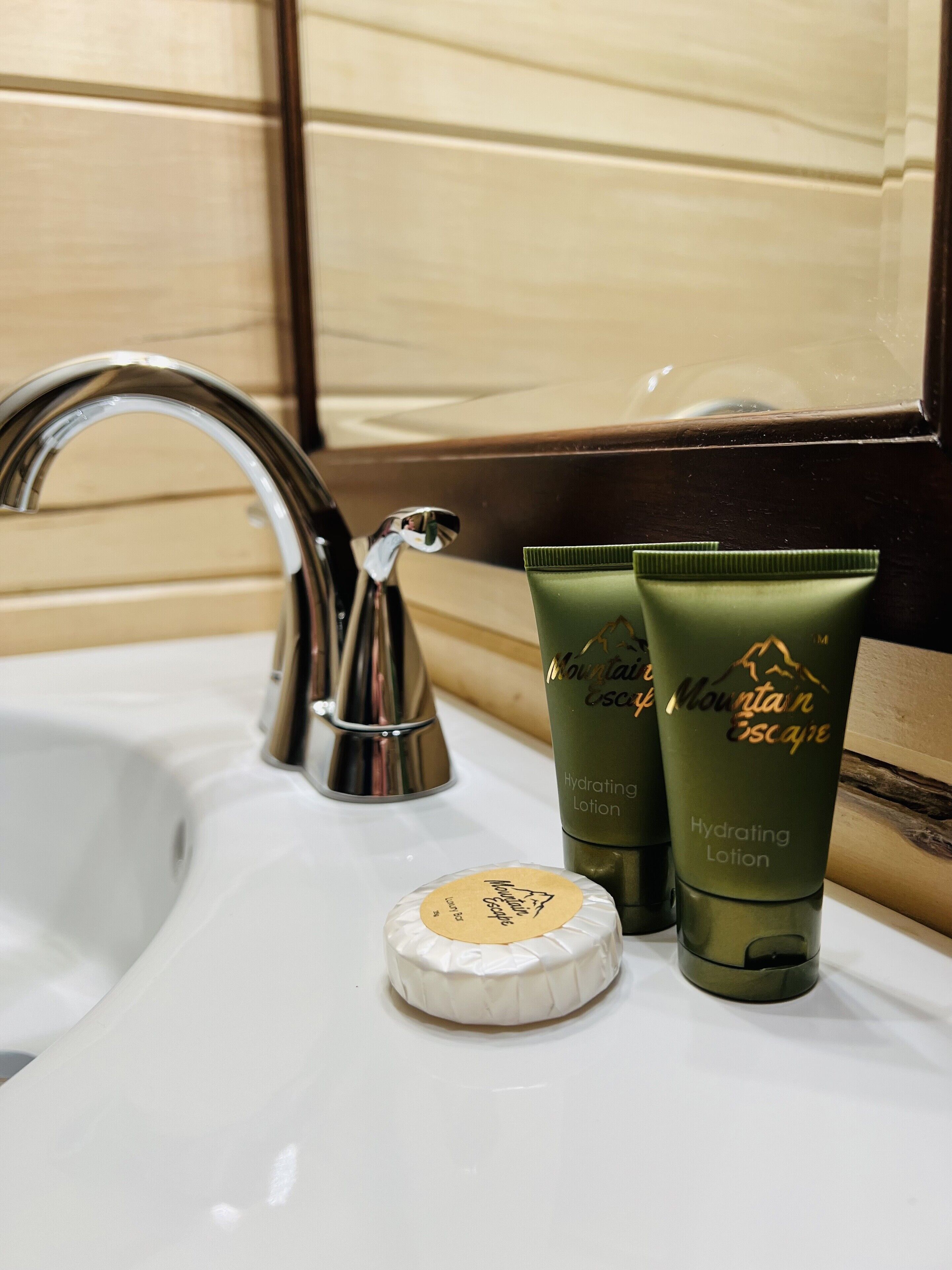 A bathroom sink with a chrome faucet, two green bottles of Mountain Escape Hydrating Lotion, and a white soap dish.