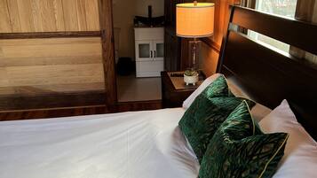 Habitación de hotel con pared revestida de madera, cama con ropa blanca y almohadas de diseño verde, mesita de noche con lámpara y vista al exterior por una ventana.