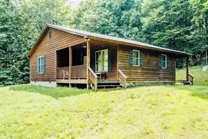 A wooden cabin with a porch, surrounded by lush greenery.