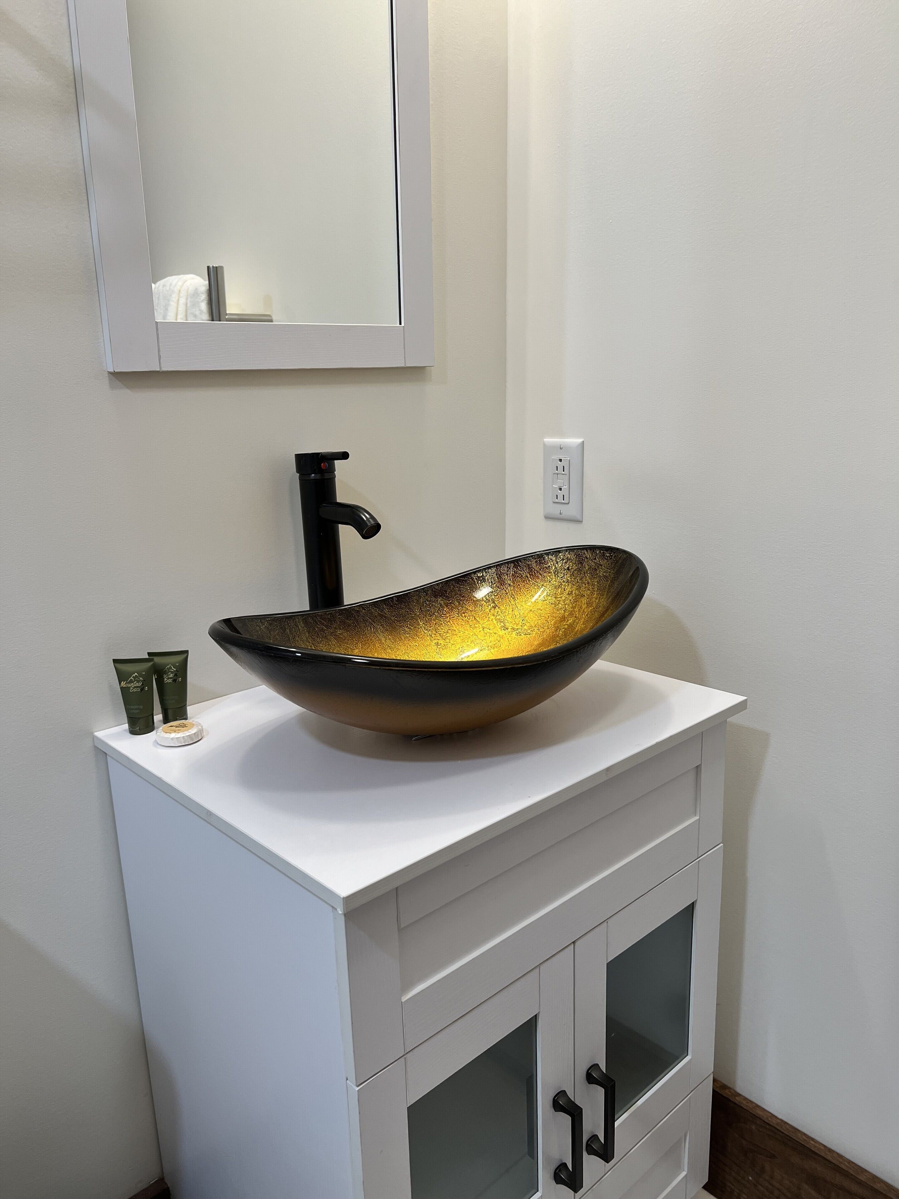 A bathroom with a white vanity, a black faucet, and a large, textured bowl sink.