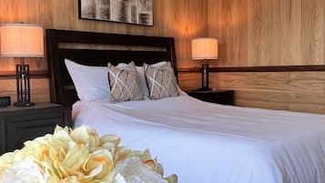 Quarto de hotel com uma cama grande, paredes de painel de madeira, duas luminárias de cabeceira e um arranjo floral grande.