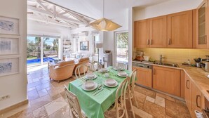 Une cuisine spacieuse avec des meubles en bois, un coin repas avec une nappe verte et une vue sur l’extérieur.