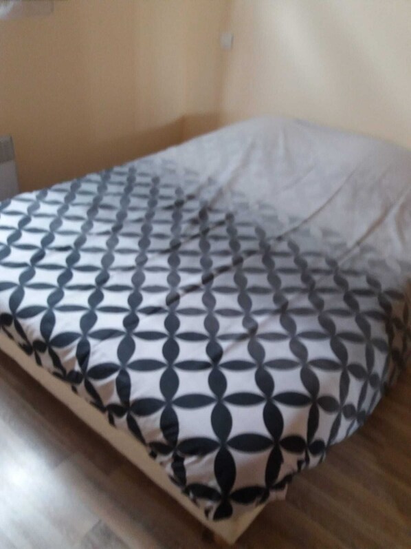 A bed with a patterned bedspread and a pillow in a room with wooden flooring and beige walls.