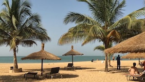 A beach with palm trees, thatched umbrellas, and lounge chairs. - Villa 88 Safari Village, Saly (Saly)