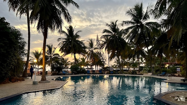 A swimming pool surrounded by palm trees and lounge chairs, with a person walking by. - Villa 88 Safari Village, Saly (Saly)