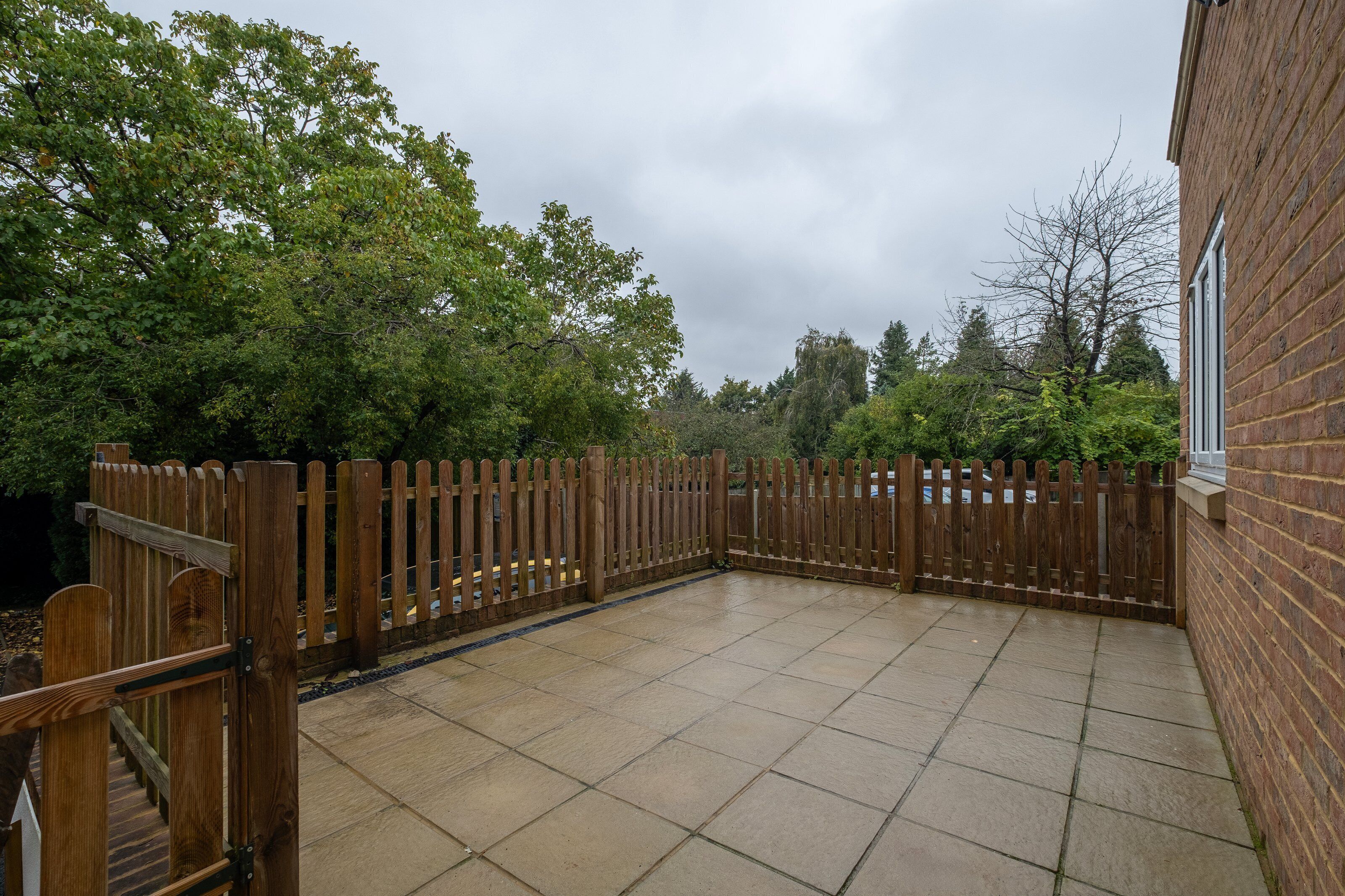 A patio area with a tiled floor, surrounded by a wooden fence and trees.