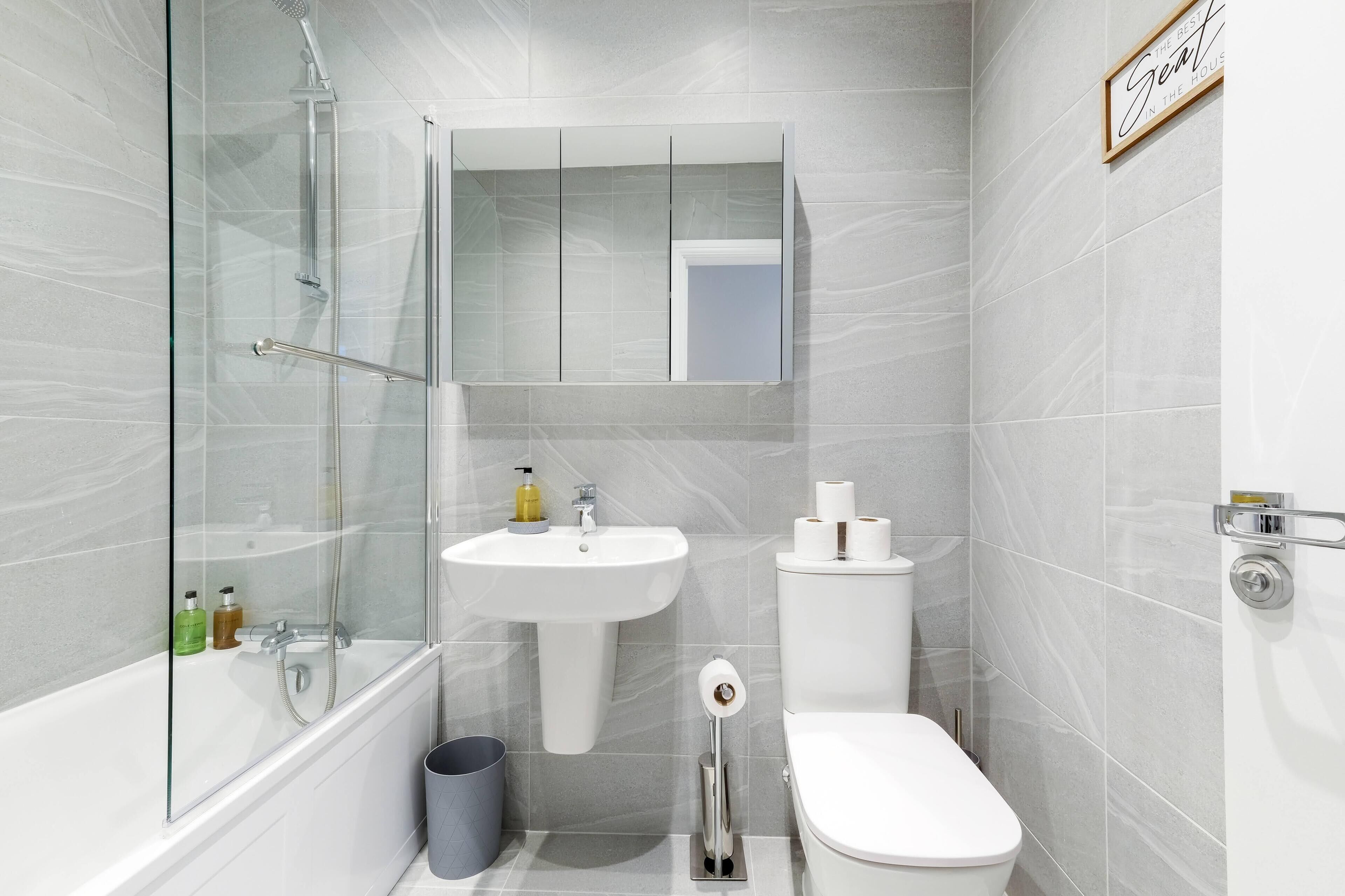 A modern bathroom with a glass-enclosed shower, a pedestal sink, a toilet, and a mirror above the sink.