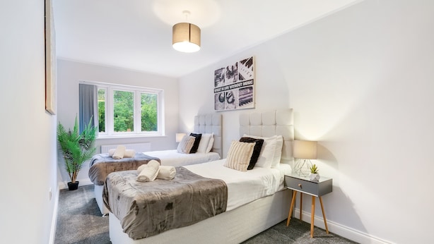 Une chambre moderne avec deux lits, une table de chevet, une lampe et une grande fenêtre.