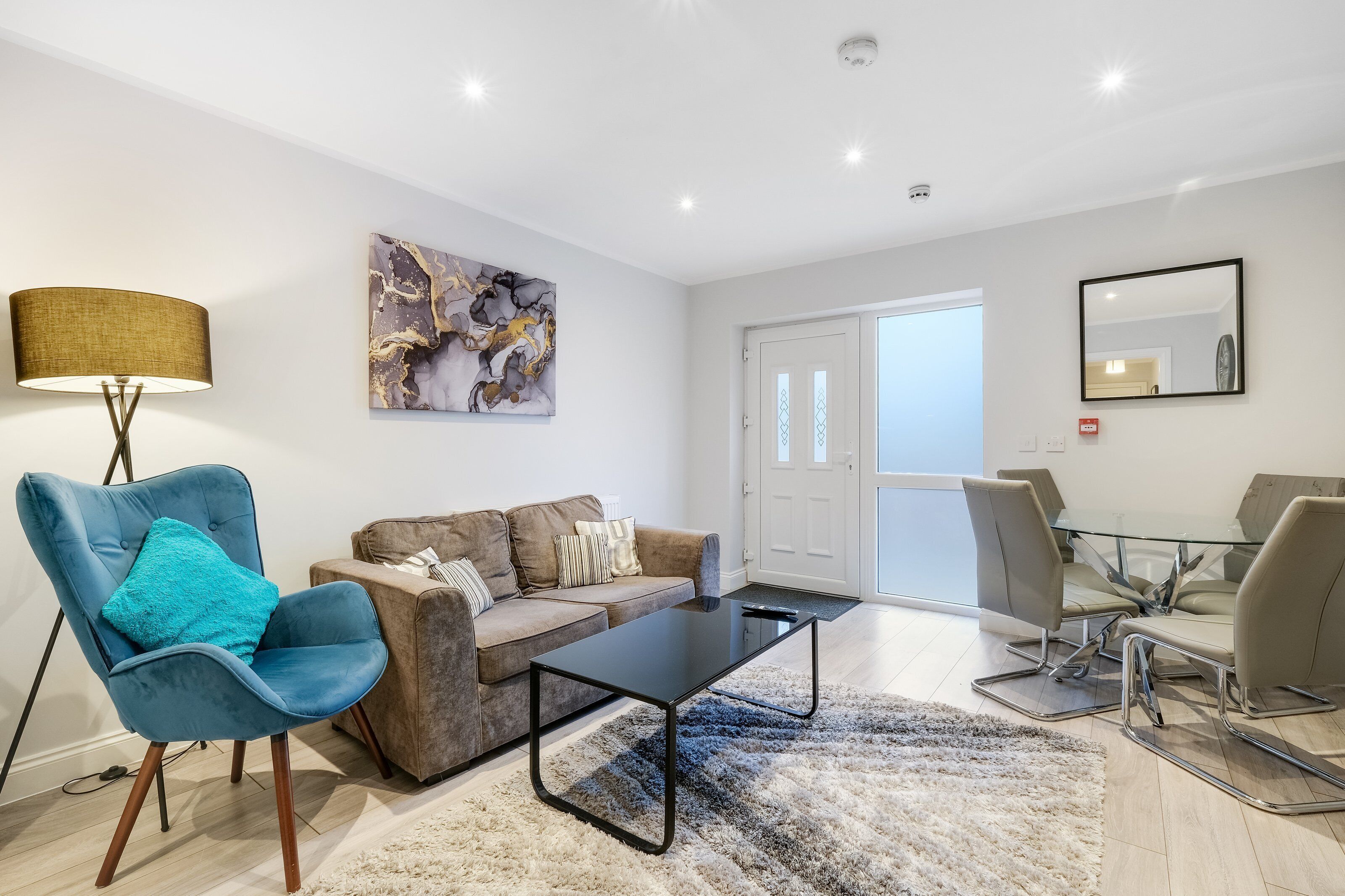 A modern living room with a sofa, a blue armchair, a glass coffee table, and a dining area with chairs.