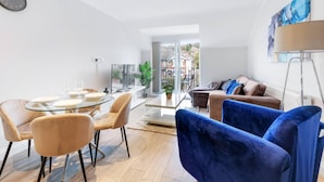 Un salon moderne avec une table à manger en verre, des fauteuils en velours bleu, un canapé et un lampadaire.