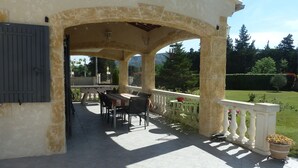 Eine überdachte Terrasse im Freien mit Tisch und Stühlen, Steinpfeilern und Blick auf einen Garten.