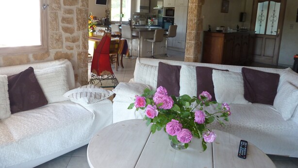 Ein gemütliches Wohnzimmer mit einem weißen Sofa, einem runden Couchtisch und einer Vase mit rosa Blumen. Ein Bogen führt in eine Küche und einen Essbereich.