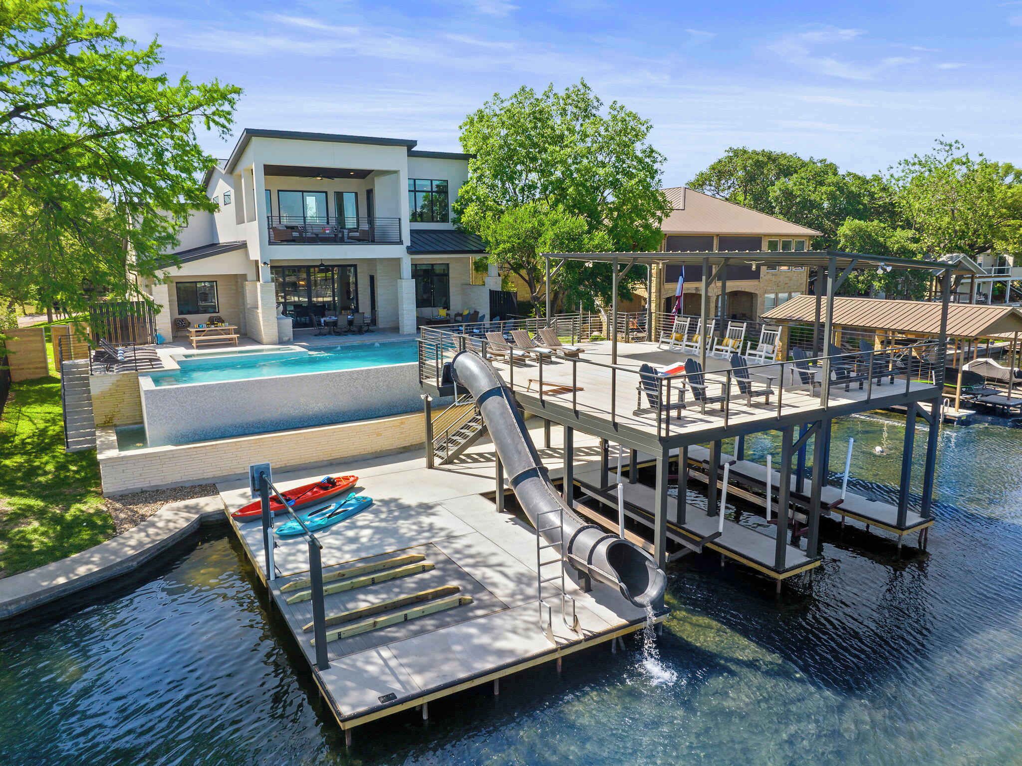 Una casa moderna con piscina, un muelle con tobogán y sillas de descanso.