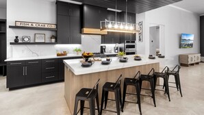 Een moderne keuken met donkere kastjes, een groot eiland met barstoelen, en een bord met de tekst 'FISH & CRAB CO'.