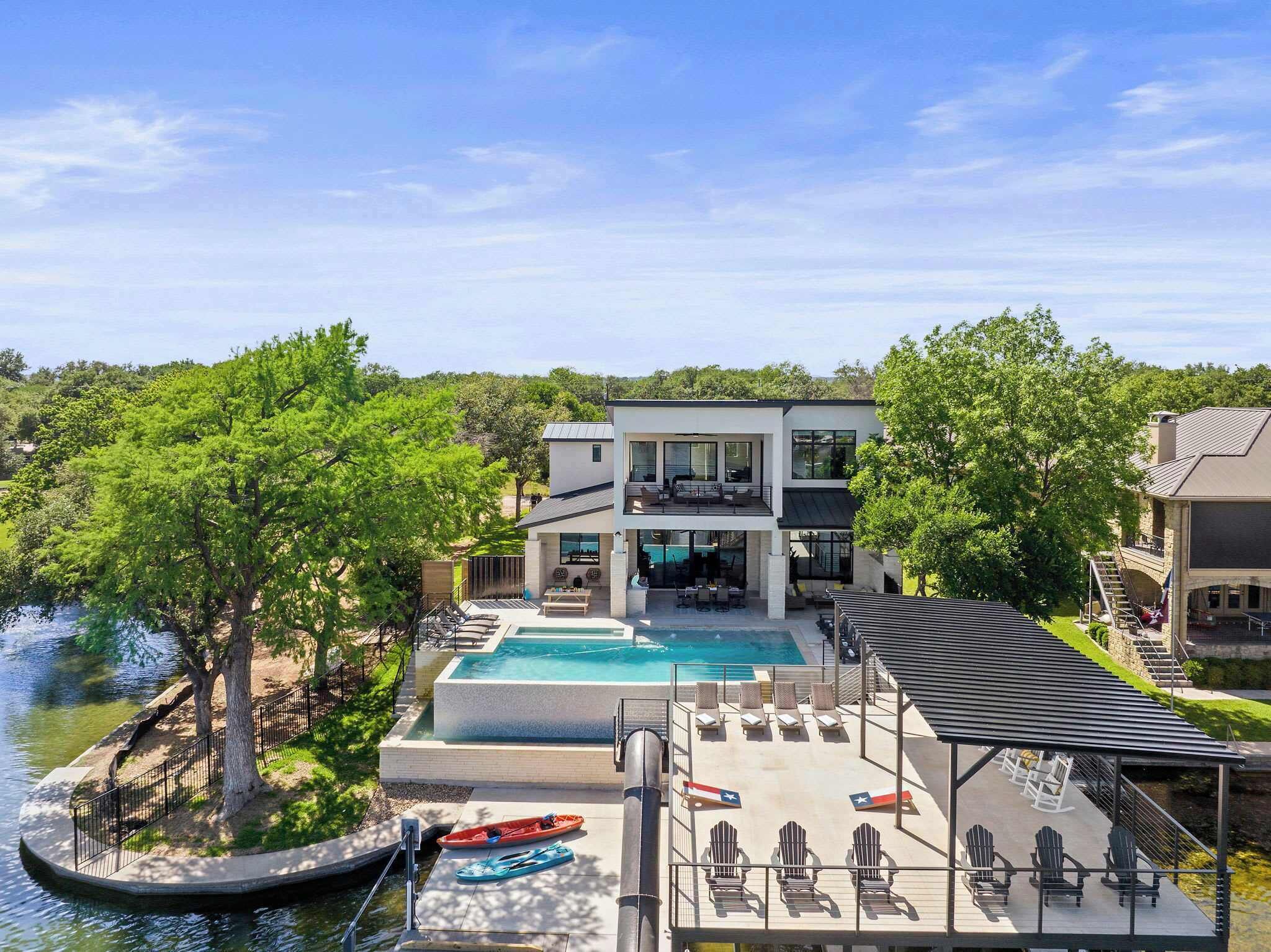 Une maison moderne à deux étages, dotée d’une piscine, d’un espace de détente extérieur et offrant une vue sur une rivière.