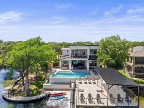 A modern two-story house with a pool, outdoor seating, and a view of a river.