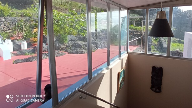 Una habitación con ventanas amplias que dan a un jardín rocoso y con plantas.