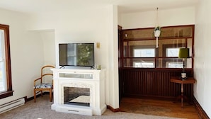Ein Wohnzimmer mit Kamin, Fernseher, Sessel und Fenster.