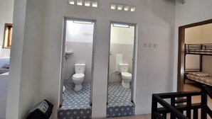 Une salle de bain avec deux toilettes, des carreaux de sol à motifs et un distributeur de gel hydroalcoolique.
