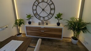 Un salon moderne avec une grande horloge murale, un meuble en bois et deux plantes en pot.