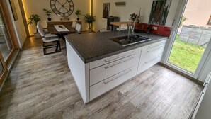 Une cuisine moderne dotée d’un îlot central, de meubles blancs et d’un coin repas avec une table et des chaises.