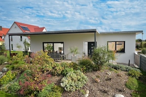 A modern house with a garden in front, featuring a patio with outdoor furniture.
