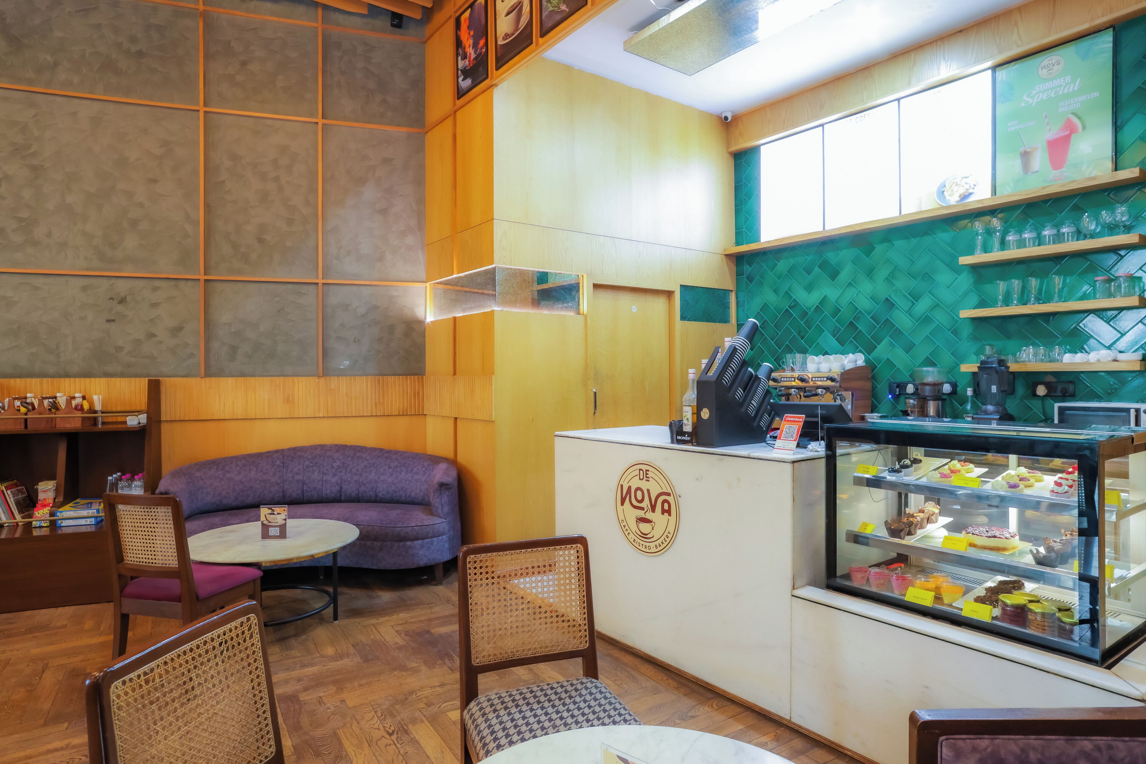 A cozy cafe interior with a seating area, a counter with a display case, and a wall-mounted menu board.