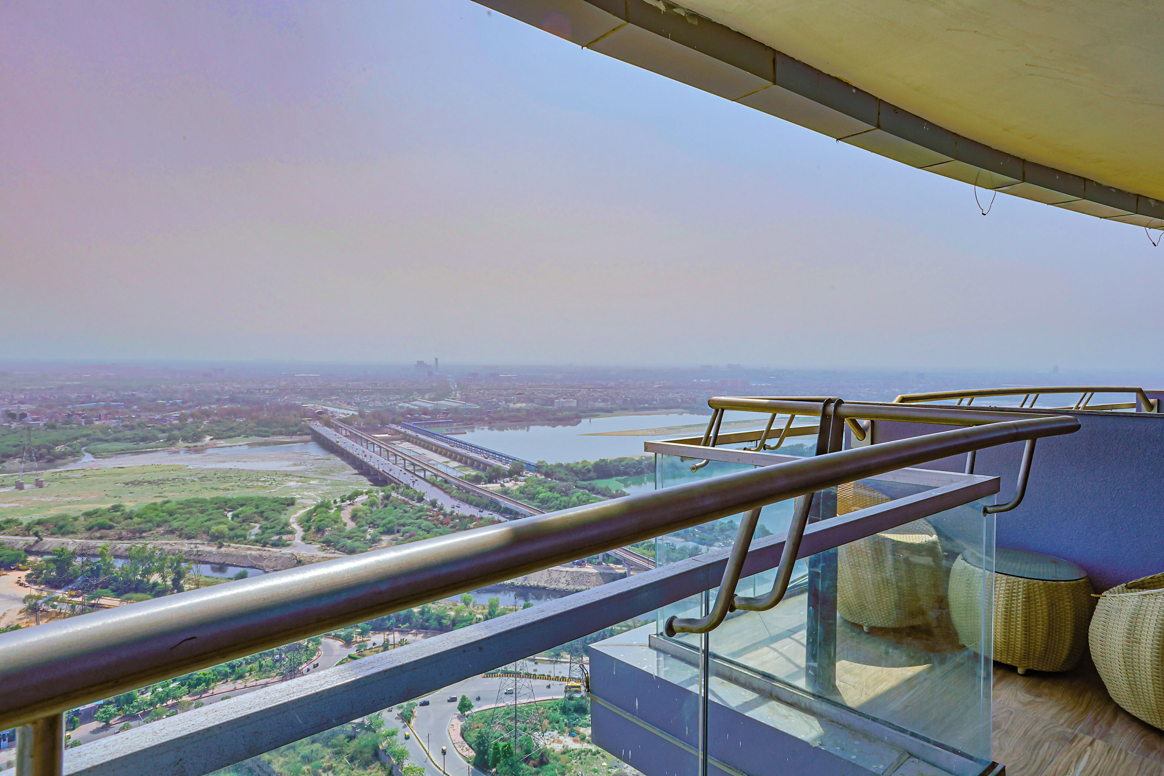 A balcony with a glass railing overlooking a cityscape, including a river and bridges.