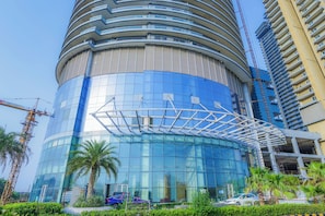A modern building with a curved glass facade, surrounded by palm trees and construction cranes. - Livbox Hotel at Supernova (Noida)