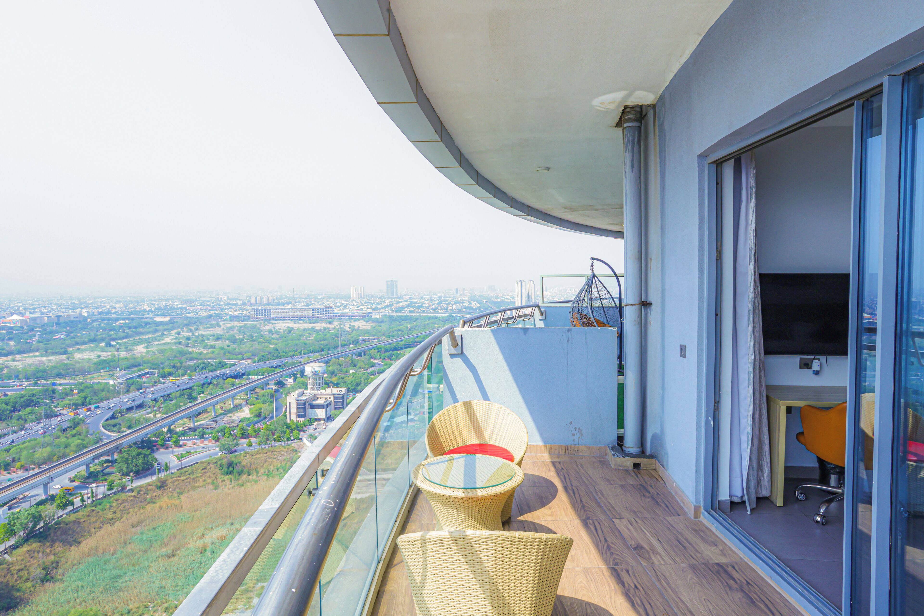 A balcony with a view of a cityscape, a glass table with chairs, and a door leading to an office area.