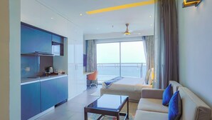 Habitación de hotel moderna con kitchenette, sofá, mesa de centro y vista al mar.