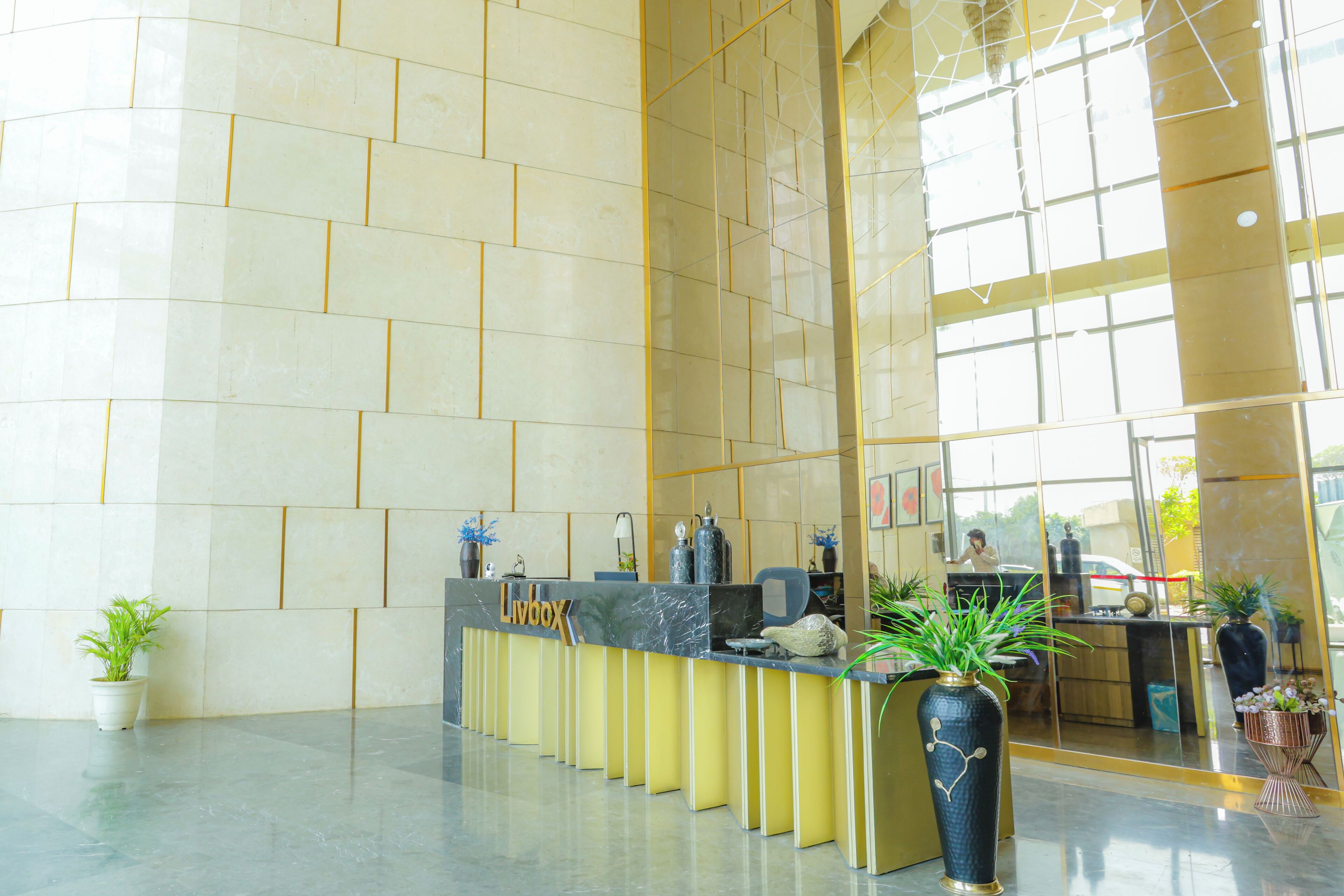 A reception desk with a 'Livox' sign, potted plants, and a glass wall reflecting interior and exterior views.