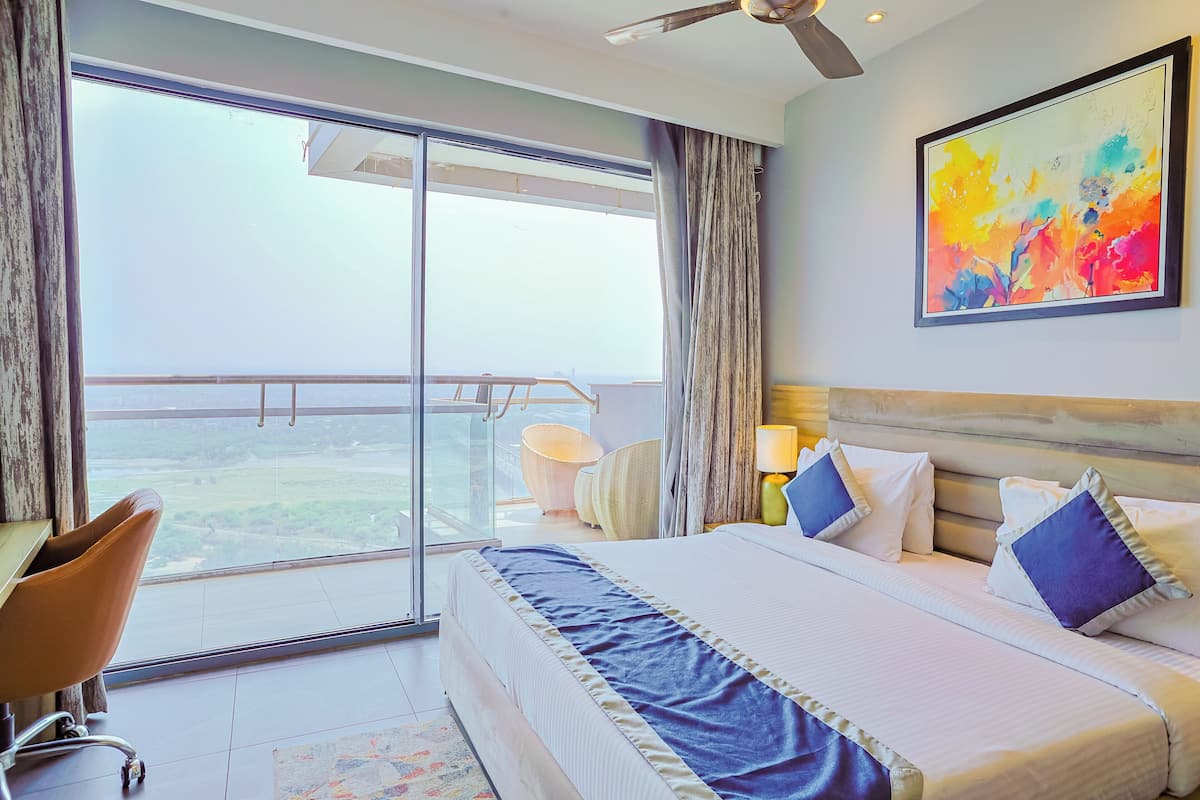 A hotel room with a large bed, a desk, a chair, a balcony with a view, and a ceiling fan.