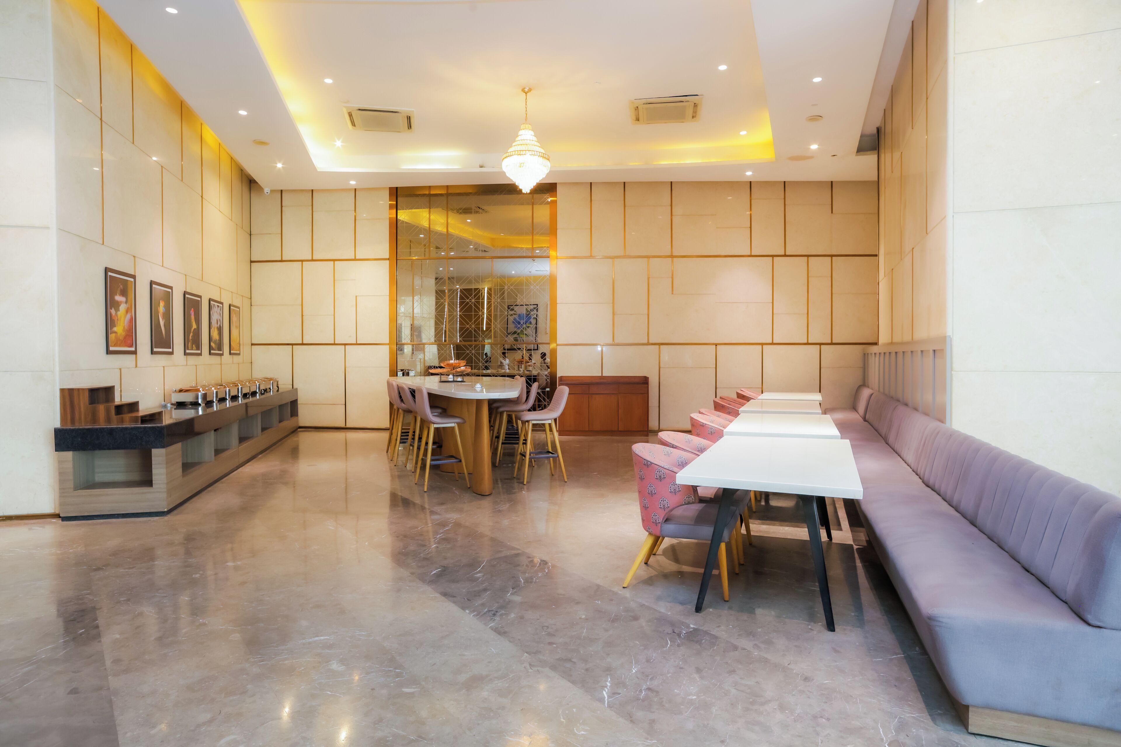 Un hall d’hôtel moderne avec un sol en marbre, un comptoir d’accueil, un espace repas doté d’une table ronde et de chaises, ainsi qu’un coin salon avec un canapé et des fauteuils.