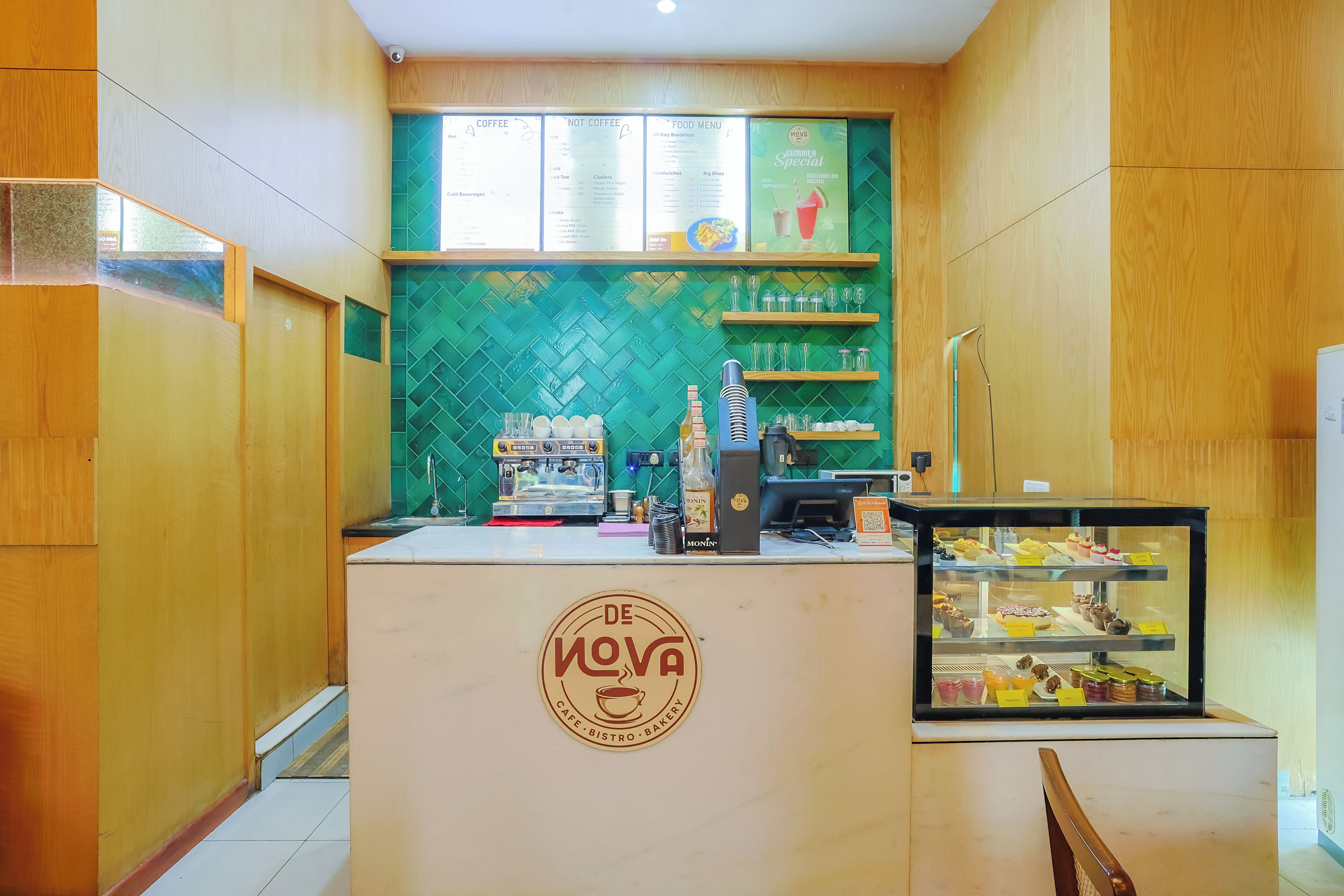 A cafe with a green tiled backsplash, a coffee machine, and a display case with pastries.