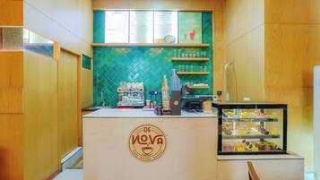 A cafe with a green tiled backsplash, a coffee machine, and a display case with pastries.